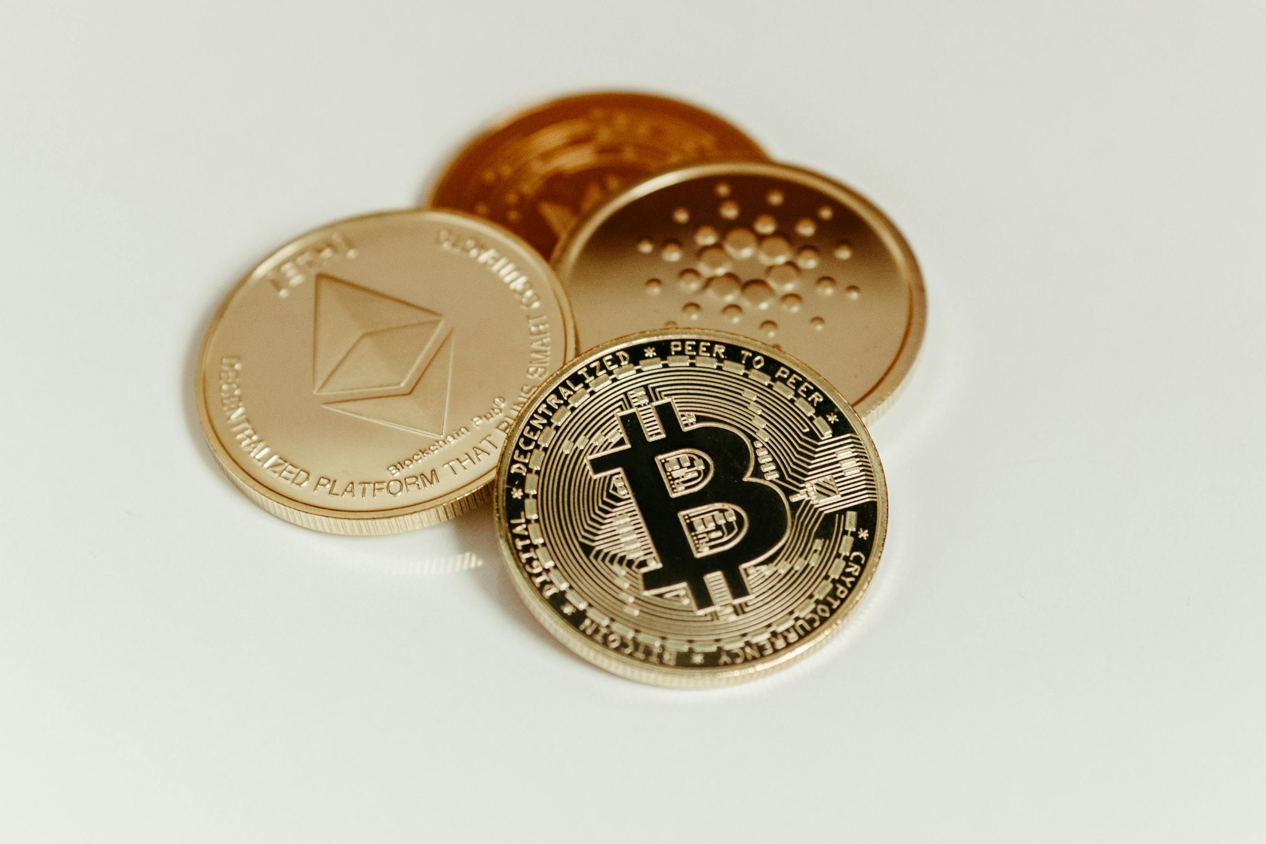 Close-up of Bitcoin, Ethereum, and Cardano coins on a plain background, showcasing digital currency.