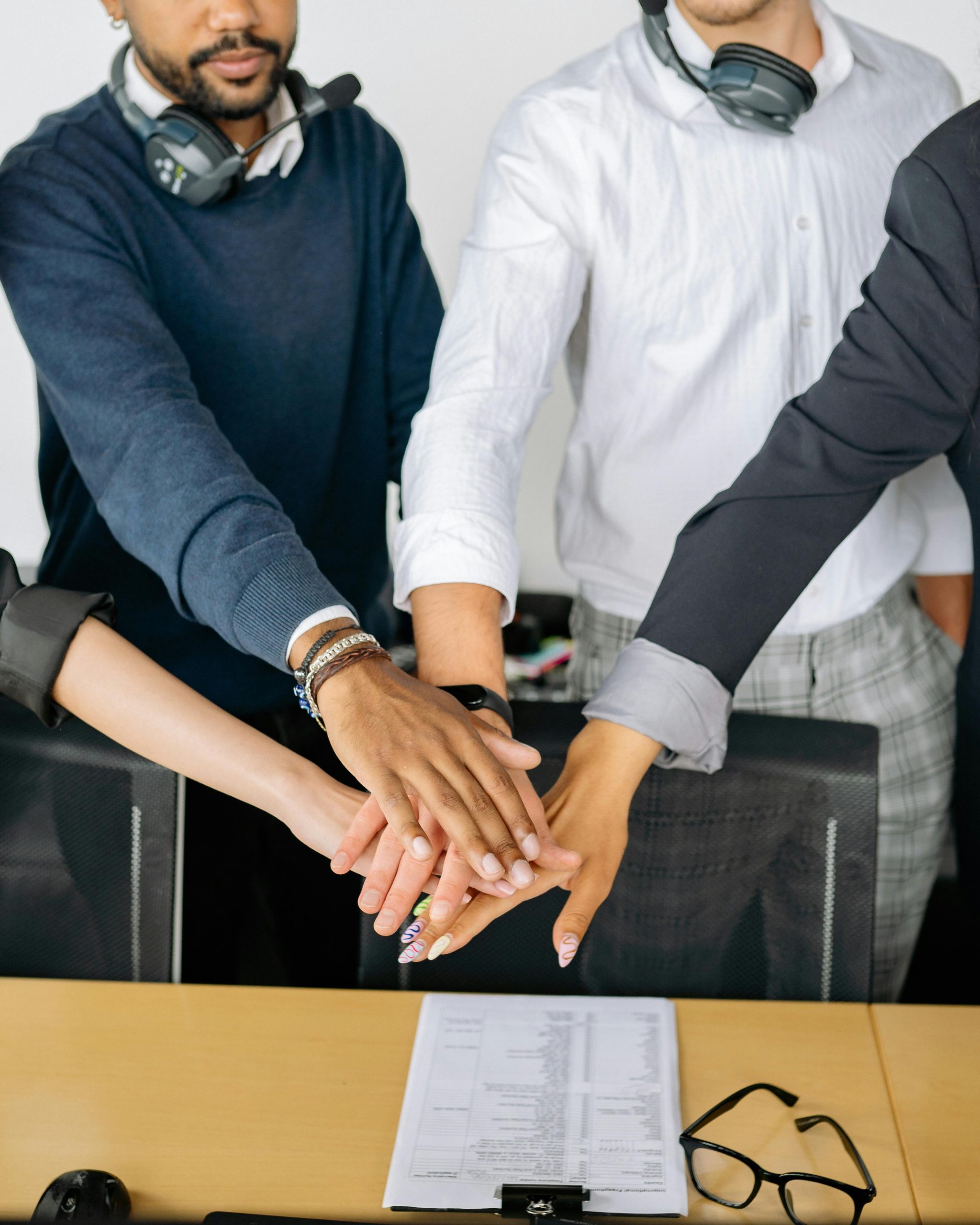 Diverse colleagues joining hands on conference table, symbolizing teamwork and unity.